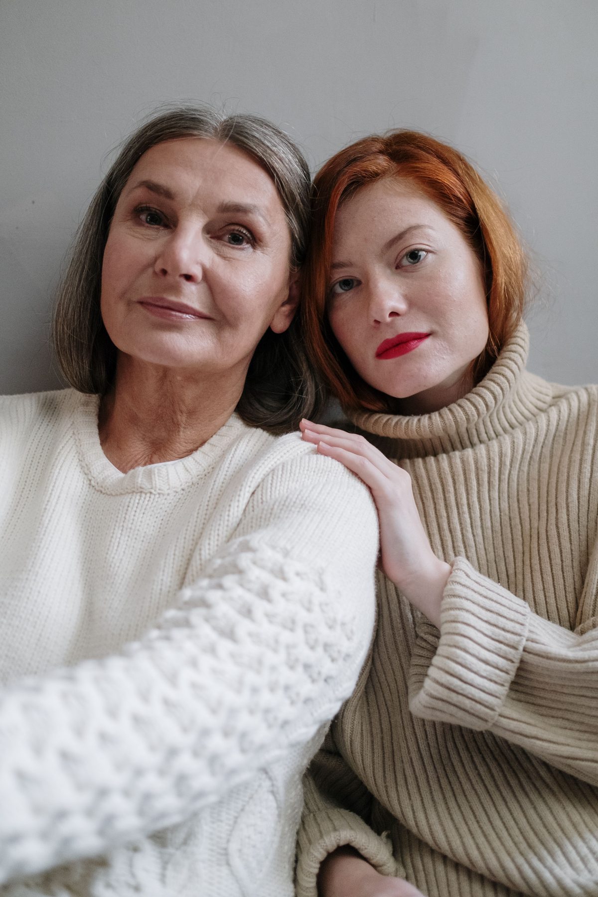A daughter and her senior mother sitting close together, smiling at home.
